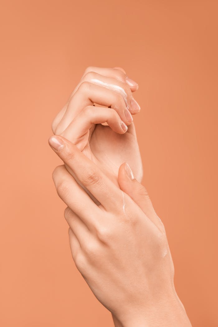 Close-up of hands with oil on peach background, emphasizing skincare and wellness.